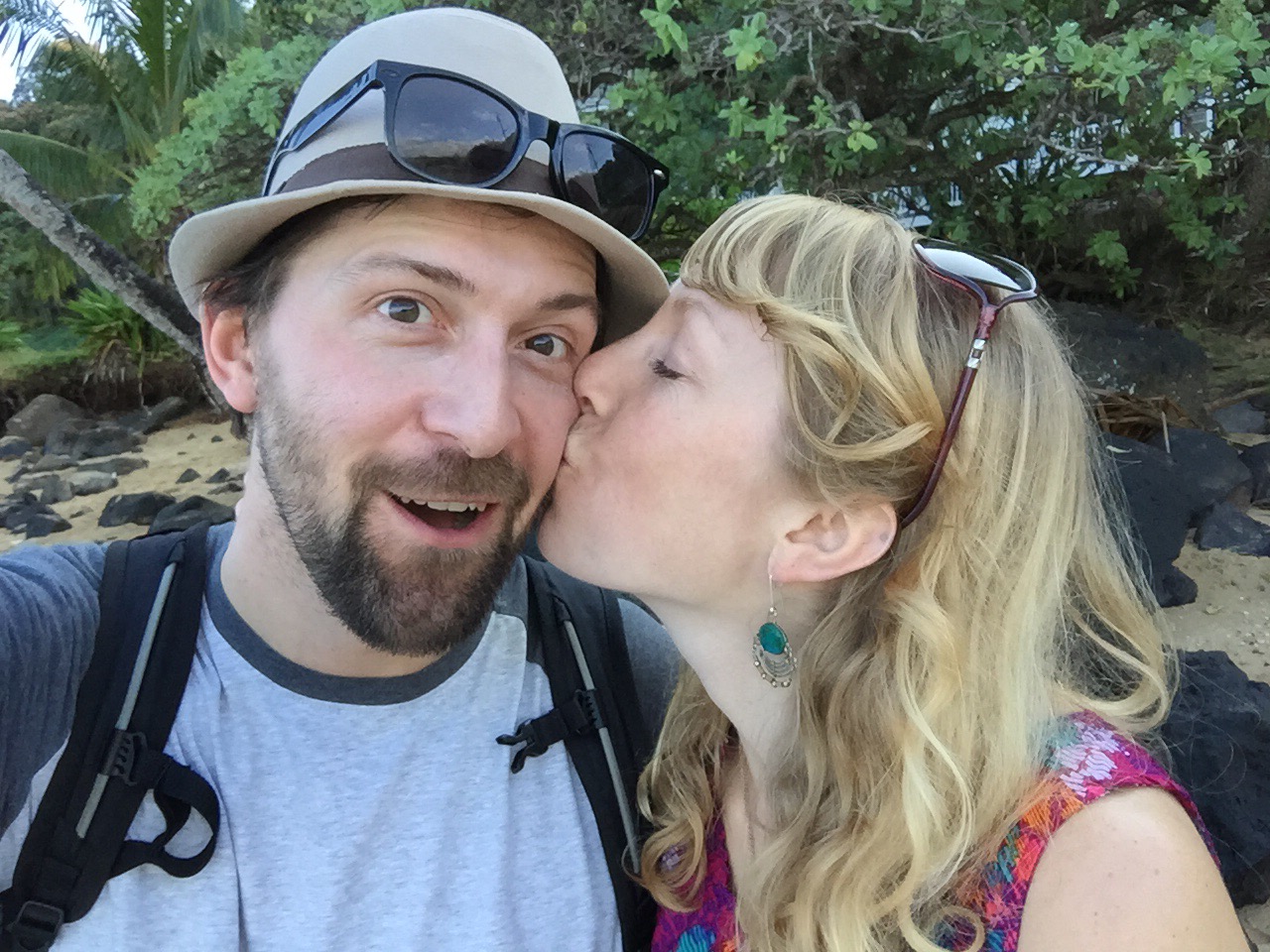 Jeff looking surprised while Andrea kisses him on cheek. They are on a beach in Hawaii.